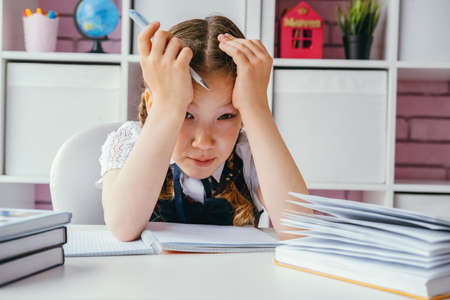 Tired sad schoolgirl girl sits at her homework