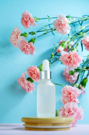 Blank transparent beauty serum dropperon a blue background with blooming pink carnation flowers. Beauty care concept advertisment poster.の写真素材