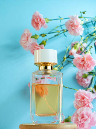 Packaging transparent glass expensive spicy fragrance perfume bottle on the background of pink carnation flowers. Perfume advertisment poster on blue.の写真素材