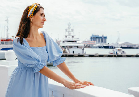 Portrait of young beautiful woman in blue dress on the shore against the background of yachts. Sea voyage concept.の写真素材