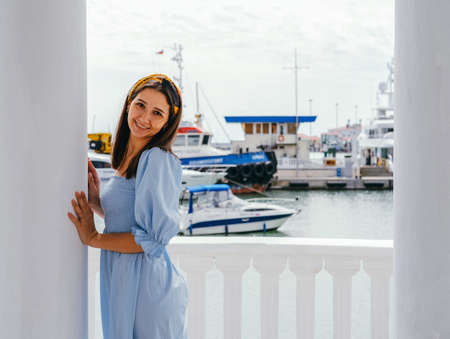 Portrait of young beautiful woman in blue dress on the shore against the background of yachts. Sea...