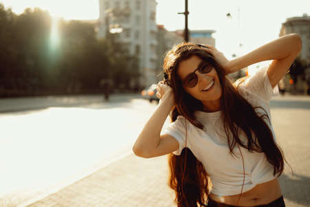 Beautiful happy young woman using cell phone and headphones and listening music in the city streets. Positive emotions, lifestyle expressive portrait in summer.の写真素材