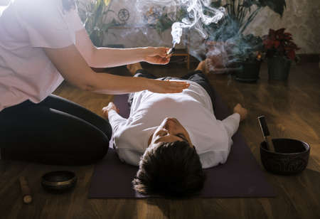 Woman holds increase over man lying on yoga mat. Esoteric massage concept.