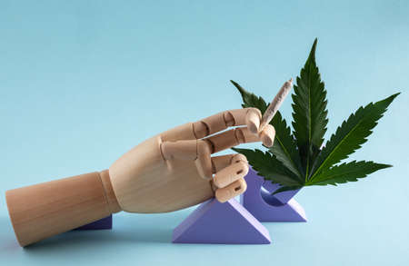 Wooden hand holding joint and cannabis leaf on blue background. smoking weed concept. art poster.の写真素材