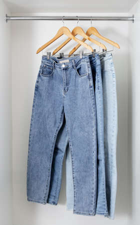 Different jeans hang on wooden hangers in white dressing room. Shopping and storage of clothes concept.の写真素材