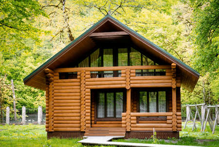 Horizontal photo of wooden house in green forest. Pros and cons of wooden house and suburban real estate concept.の写真素材