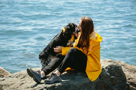 Young beautiful woman in yellow raincoat hugging her spaniel dog sitting on sea coast. Travel with pet concept.の写真素材