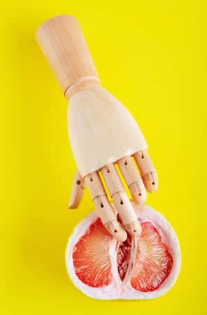 Wooden hand with half of grapefruit on yellow background.の写真素材