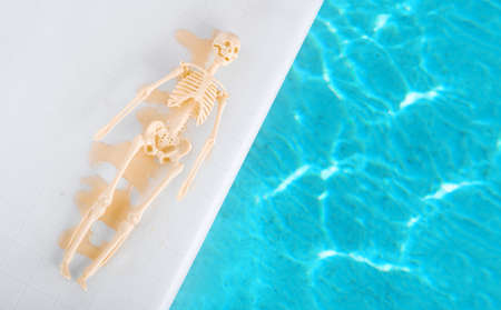 Humor concept of hot weather in summer. Man melted from heat by pool. Skeleton is lying on the side of the pool.の写真素材