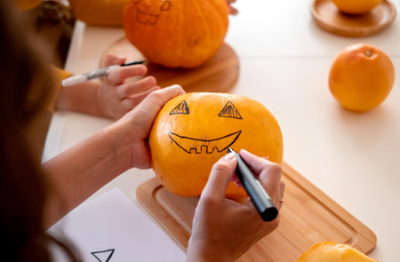 Close up female hands with black marker drawing spooky face on pumpkin. Halloween party preparations.の写真素材