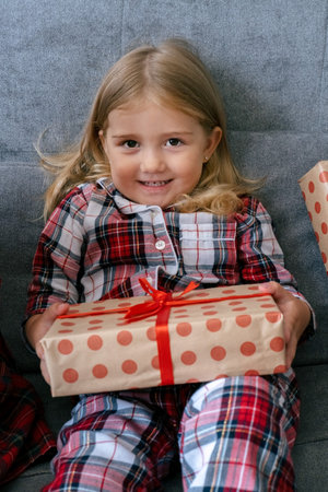 Cute lifestyle portrait little girl sitting on couch with present box. Expressive happy kid.の写真素材