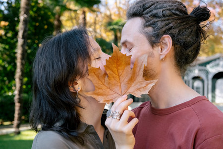 Couple kisses and closes with maple yellow leaf in autumn park, romantic happy date. Concept of love, relationship, privacy.の写真素材