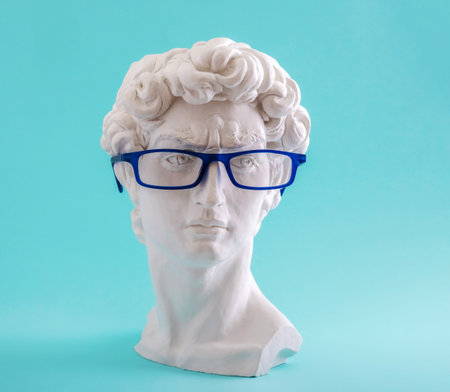 Plaster statue head wearing blue glasses on blue background.の写真素材
