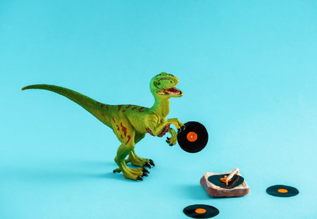 Cute green dinosaur toy holding a vinyl record and listen vinyl on vinyl record player on a blue background.の写真素材