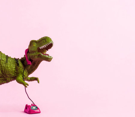 Cute green toy dinosaur speaking on retro phone on pink background. copyspace.の写真素材