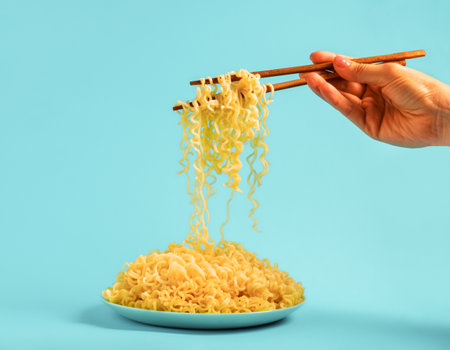 Egg noodles on blue plate and female hands with chopsticks on blue backgroundの写真素材
