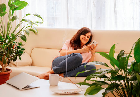 Young woman sitting on sofa in the morning in white modern apartments.の写真素材