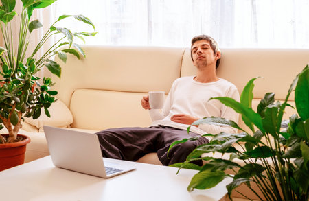 Young man with coffee cup relaxing on sofa. Coffee break on remote work from home concept.の写真素材