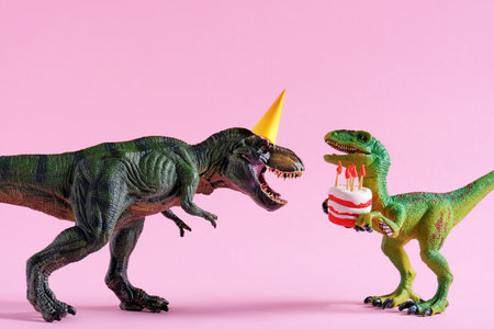 Cute happy green dinosaurs in birthday hats holding cake with flaming candles on pastel pink background. copyspace. Minimal art birthday card idea.の写真素材