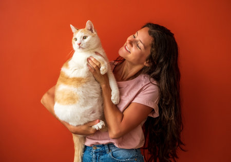 Happy young brunette caucasian woman holding her white and red cat on orange background.の写真素材