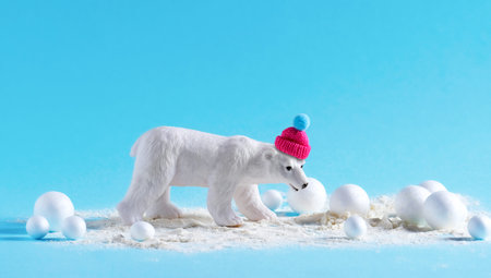 Cute little model of white bear in knitted hat with snowballs on blue background. Creative minimal concept.の写真素材