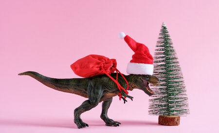 Dinosaur in Santa Claus hat holding bag with presents on pink background. Minimal art poster for winter holidays sale.の写真素材
