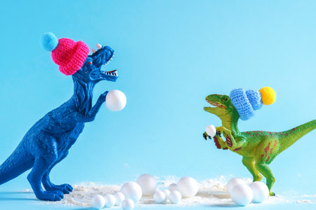 Two cute dinosaurs in knitted hats build snowman. Cute funny winter holidays creative poster.の写真素材