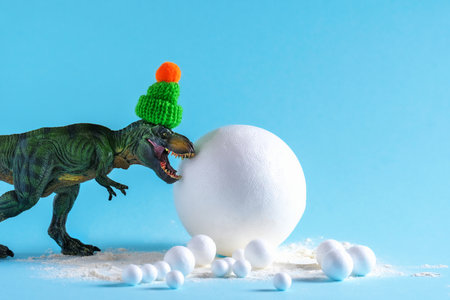 Cute green dinosaur with big snowball on blue background. Funny winter holidays card.の写真素材