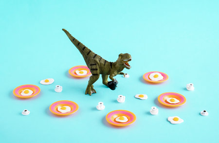 Green dinosaur with fried eggs and coffee cups on blue background.の写真素材