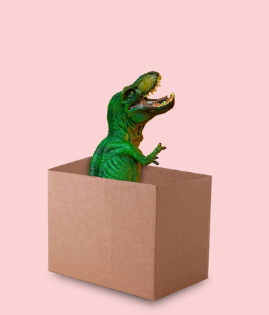 Funny green dinosaur sticks out of cardboard box on pink background. Funny minimal greeting card.の写真素材