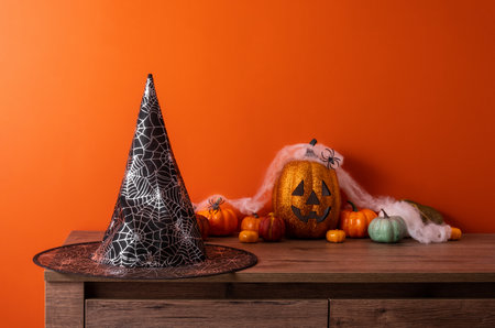 Witch hat and pumpkins on wooden chest of drawers opposite orange wall. Space for text. Greeting card hello autumn.の写真素材