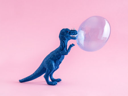 Happy blue toy dinosaur with blue chewing gum bubble on pink background.の写真素材