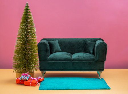 Emerald green couch, green carpet and Christmas tree with presents on pink wall and beige floor.の写真素材