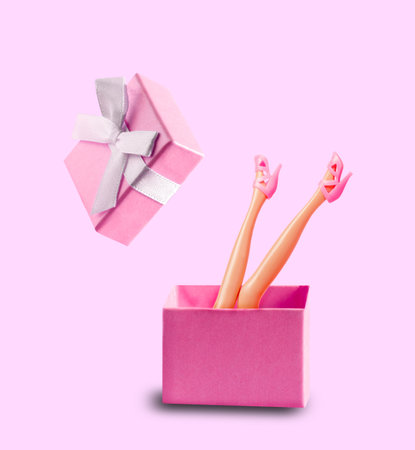 Doll's feet in pink shoes stick out of pink gift box on pink background.の写真素材
