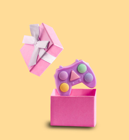 Pink game joystick flies out of pink gift box on a yellow background. Video console as gift concept. Postcard for holidays. Minimal art.の写真素材