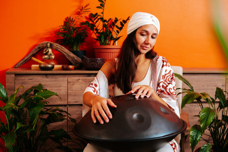 Beautiful young woman in white turban playing handpan musical instrument. Sound healing concept.の写真素材