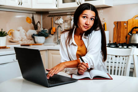 Tired woman is working at computer and answering work call at home in the kitchen.の写真素材