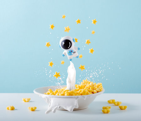 Cute little astronaut is levitating over plate of cornflakes with milk on blue background. Creative breakfast concept.の写真素材