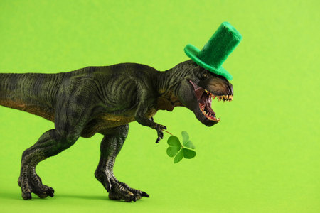 Green dinosaur in green hat holds leaf of clover.の写真素材