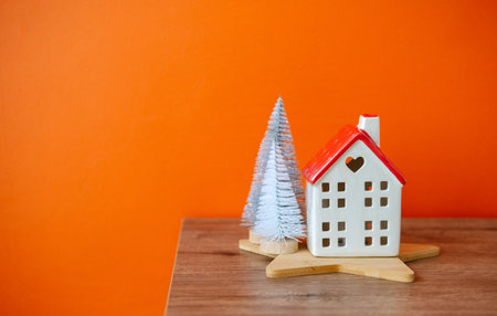 Cozy composition with white ceramic house and fir trees on wooden table on a background of orange wall.の写真素材