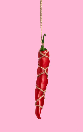Red hot pepper tied with jute rope on pink background. Shibari concept.の写真素材