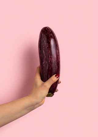 Woman's hand holds eggplant on pink background.の写真素材