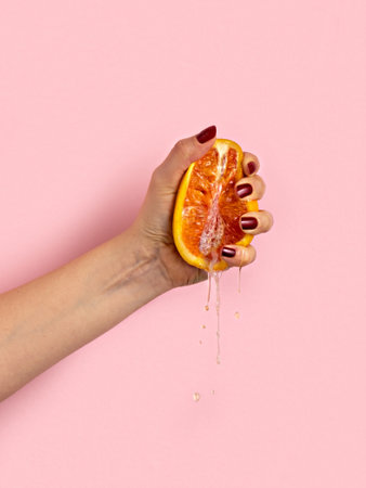 Female hand with half of juicy orange on pink background. Sex concept.の写真素材