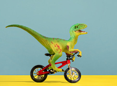 Cute happy green dinosaur riding bike on blue and yellow background.の写真素材