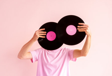 Portrait of man in pink shirt holding two vinyl records near his face on pink background.の写真素材