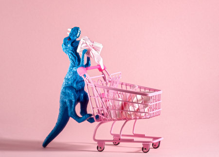Funny blue dinosaur toy with shopping cart full of present boxes on pink background.の写真素材