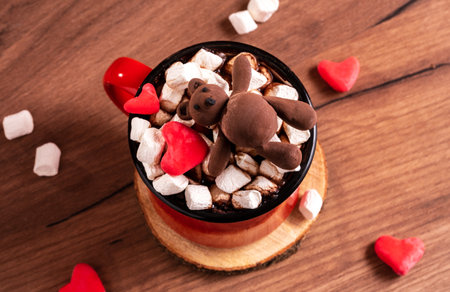 Top view mug with a hot drink with marshmallows decorated with a chocolate bear and candy heartsの写真素材