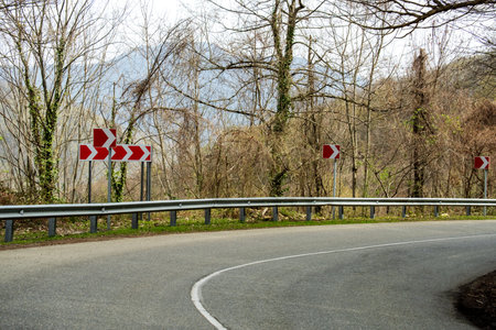 Sharp turn and warning signs in mountainous terrainの写真素材