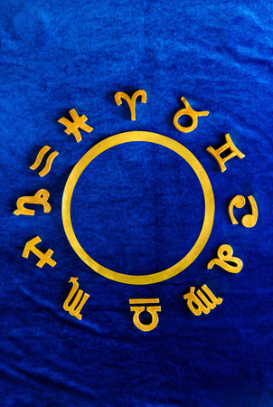 Zodiac wheel with golden figures of zodiac signs on blue velvet. Top view flat lay.の写真素材