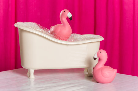 Funny pink flamingoes and bath with soap foam on a pink background.の写真素材